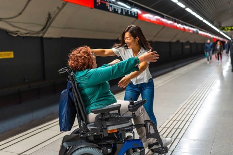 Happy disabled woman meeting a chinese female friend in the metro platform smiling and embracing