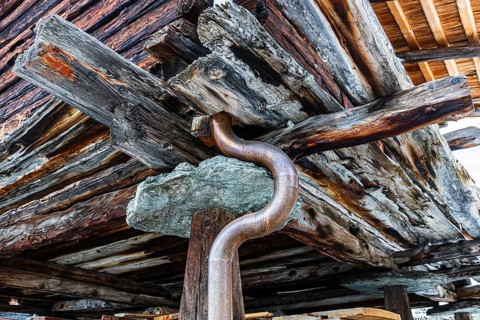 Old weathered hay barn with wooden support, stone slab and copper pipe, Chandolin, Val d'Anniviers,