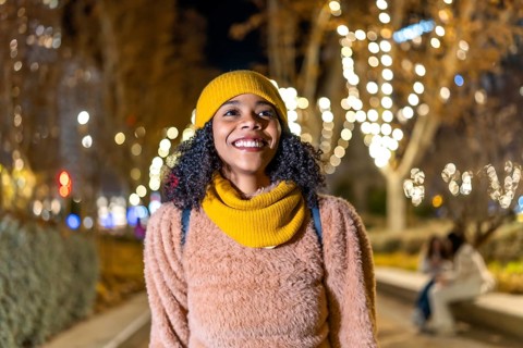 Portrait of a young woman wearing winter clothes, enjoying christmas lights in a decorated city at