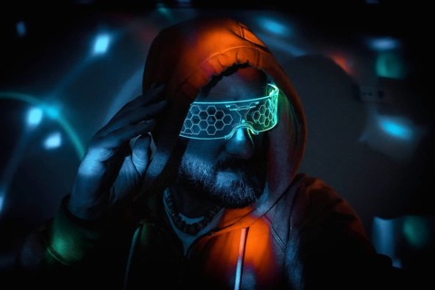Bearded man wearing futuristic neon glasses and hoodie, touching his head, immersed in a cyberpunk,