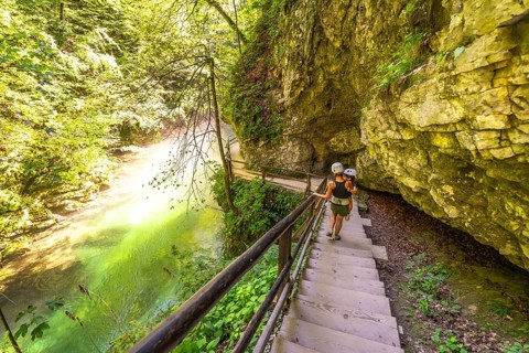 Tourists wearing helmets are walking down wooden stairs along the radovna river in vintgar gorge, a