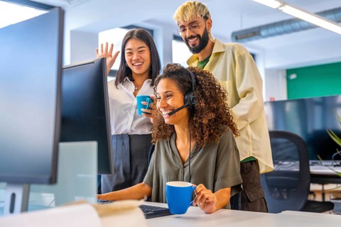 Coworkers drinking coffee and waving while making a video call suing headset