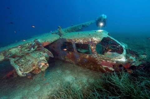 Diver looking at Cessna aircraft wreck underwater on the seabed while scuba diving, Porto Azzurro,