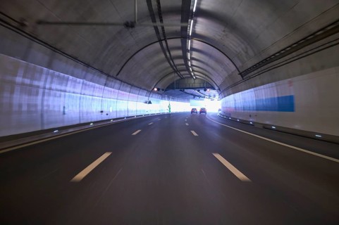 Modern, well-lit motorway tunnel with blue illuminated walls and a clear asphalt road, Switzerland,