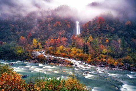 Waterfall with river Verzasca surrounded by autumn coloured deciduous trees, rainy and foggy