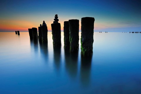 Stone pyramids on old groynes with algae in the water on the beach of the Baltic Sea, long exposure