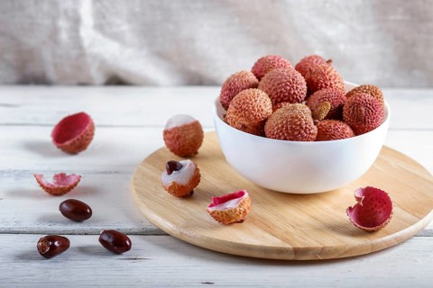 Lychee in a white plate on a white wooden background, close up