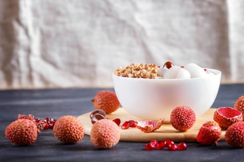 Greek yogurt with lychee, pomegranate seeds and granola in a white plate on a black wooden