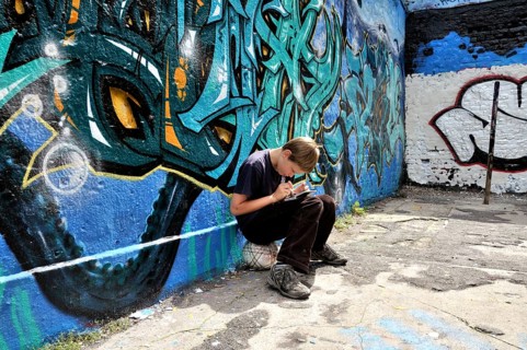 Ten-year-old boy playing with his Nintendo in front of a graffiti wall, football pitch, Germany,