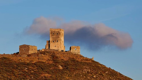 Sunset colours the clouds over the imposing ruins of a fortress on a mountain, residential tower on