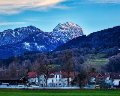 Idyllic village view with snow-covered Mount Wendelstein in the background and a green meadow under