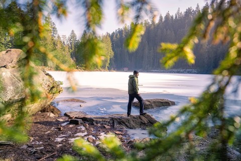 Man photographed through branches at the frozen lake, surrounded by forest and rocks, Glaswaldsee,