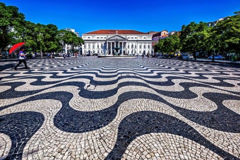 Wavy black and white patterned pavement in a sunny urban square with people and classic building in