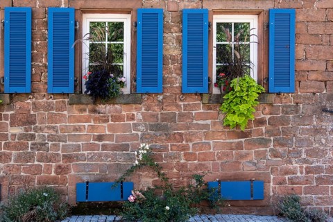 Rustic house façade with windows, blue shutters and flowering plants, Weyher, Southern Palatinate,