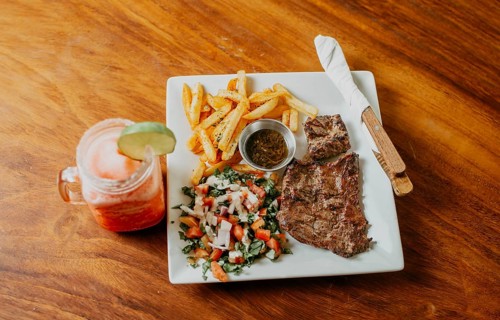 Plate of skirt steak with french fries and drink served on wooden table. Delicious homemade steak