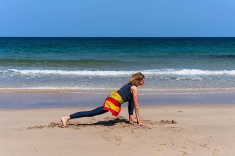 A woman doing yoga on a sandy beach by the sea. Ashwa Sanchalanasana or Sprinter, variant. Treen