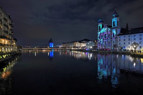 Water tower and Jesuit church on the right with light installation, on the Reuss at dusk, Old Town,