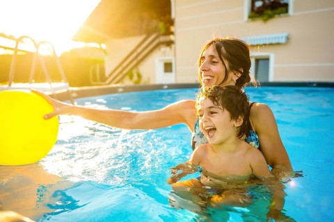 Happy mother and son laughing and playing with a yellow inflatable ball in a home swimming pool