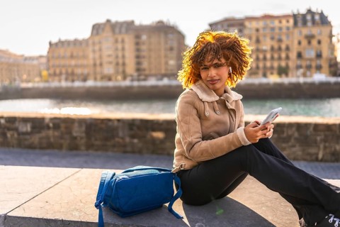 Side view with copy space of a latin beauty woman using phone sitting next to the river at city