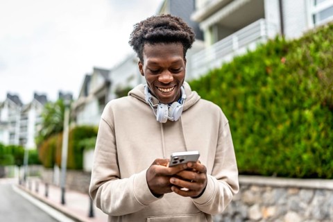 Confident african young man smiling while using phone standing in a residential street