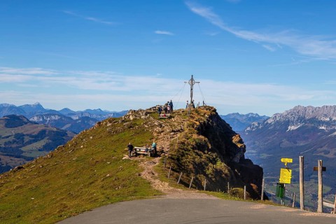 Hiking on the Kitzbüheler Horn in Tyrol: summit cross with a view on a pre-summit just below the