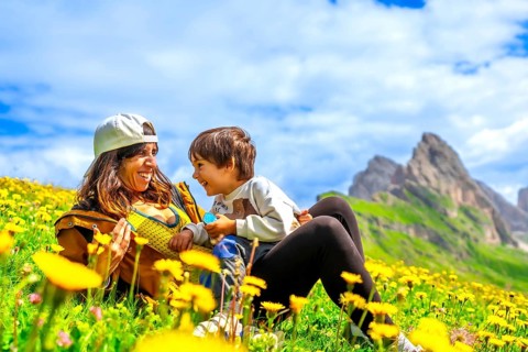 Mother and son relaxing in a dandelion field, enjoying the breathtaking view of the seceda
