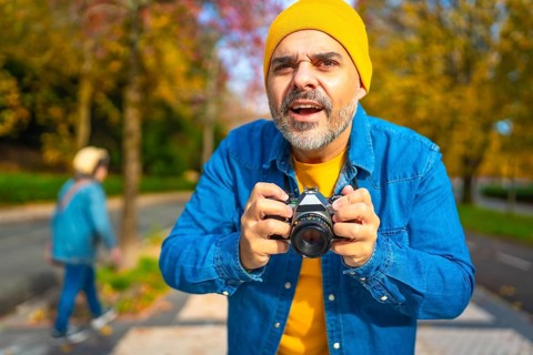 Surprised mature caucasian man holding digital camera about to photographing in the city in autumn