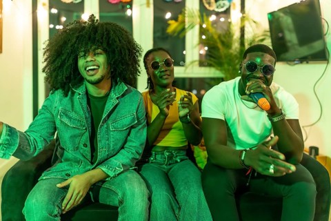 Three young multiracial people sitting on the sofa enjoying karaoke together at night