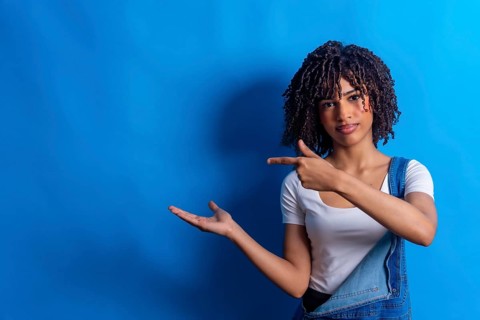 Young woman pointing her finger to the side and showing something with her open hand on a vibrant