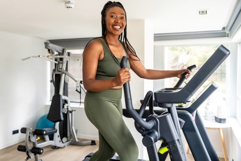 Happy african american woman exercising on elliptical cross trainer in bright home fitness room