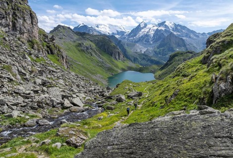 Hiker in front of mountain stream and mountain lake Lac de Louvie with glaciated summit of the