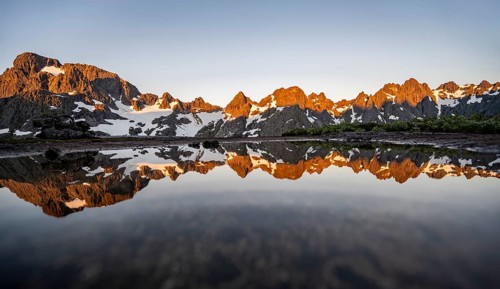 Rocky mountain peaks reflected in a small pond, mountain landscape with alpenglow at sunrise, at