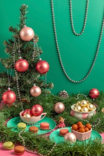 Table scene with small Christmas tree, pink baubles and macaroons, surrounded by green branches