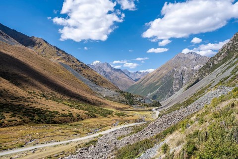Gravel track in a valley, picturesque mountain landscape with white mountain peaks, Tian Shan