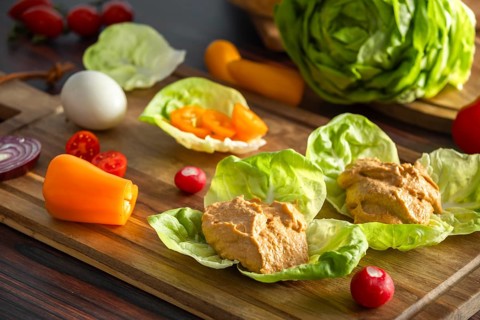 Leaf salad with hummus and fresh vegetables, including peppers and radishes, on a board