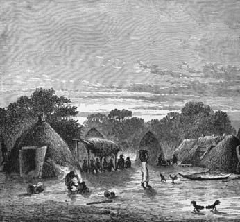 Village view with huts in the tropics, locals sitting in the shade, woman carrying a bowl on her