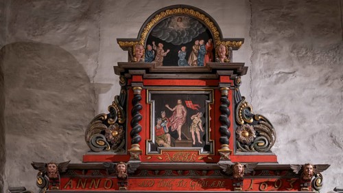 Close-up, richly decorated wooden altar in front of a stone wall, decorated with images of saints,