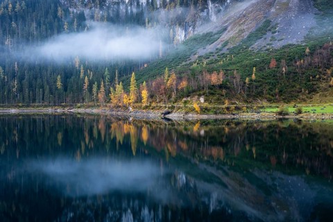 The Vordere Gosausee in autumn. Part of the path around the lake, with a cloud. Trees in autumn