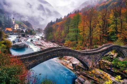 Stone bridge Ponte dei Salti over river Verzasca on a rainy autumn day, behind it village view