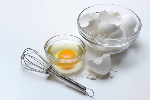 Egg whites and egg yolks in glass bowl and egg shells, whisk