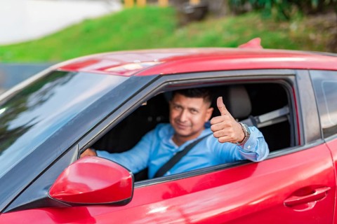 Smiling driver in his car giving a thumbs up. Male driver showing thumbs up while driving