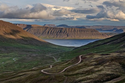 Winding gravel road, mountain road, fjord and mountains behind, cloudy mood, summer, Westfjords,