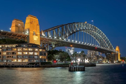 Sydney Harbour Bridge at night, illuminated at blue hour, with city lights in the background and