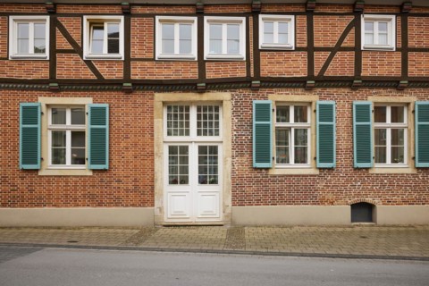 Facade of a half-timbered brick house with white windows, a mighty entrance door and blue-green