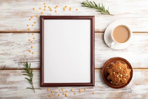 Brown wooden frame mockup with cup of coffee and cake on white wooden background. Blank, top view,