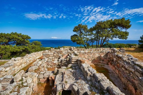 Ancient ruins with stone walls and views of the sea and trees under a blue sky, Kamiros,