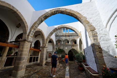 Historic monastery courtyard with stone arcades and bright white walls. Tourists explore the