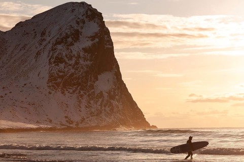 Surfer with surfboard under his arm on the beach of Unnstad, winter surfing, Lofoten Island