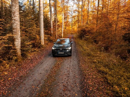 Car standing on a forest path, surrounded by autumn trees and leaves, electric car, VW ID5,