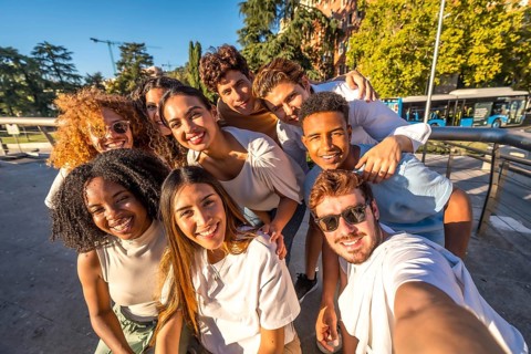 Multiracial group of happy young friends taking selfie together at street during sunset